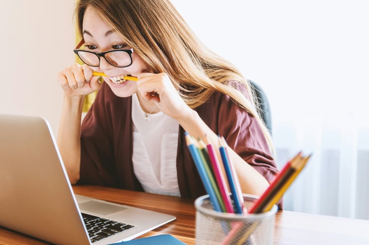 Woman is feeling tax season stress and is biting a pencil while sitting in front of a computer.